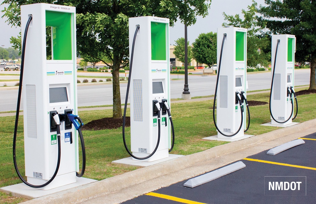 En rad med fyra vita laddstationer för elbilar med gröna detaljer från Electrify America, installerade på en betongplatta bredvid parkeringsplatser.