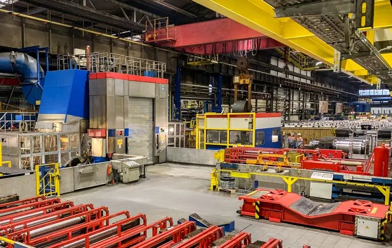 Överblick över en stor verkstad med tunga maskiner, transportband och traverskranar.