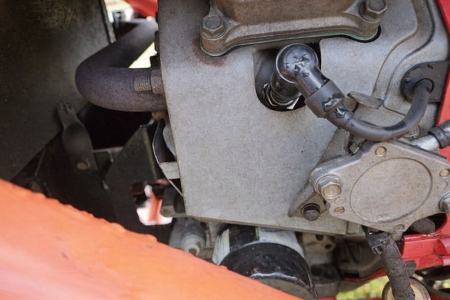 Detaljbild av en bilmotor med tändstift och kablar, synlig oljefilter undertill.