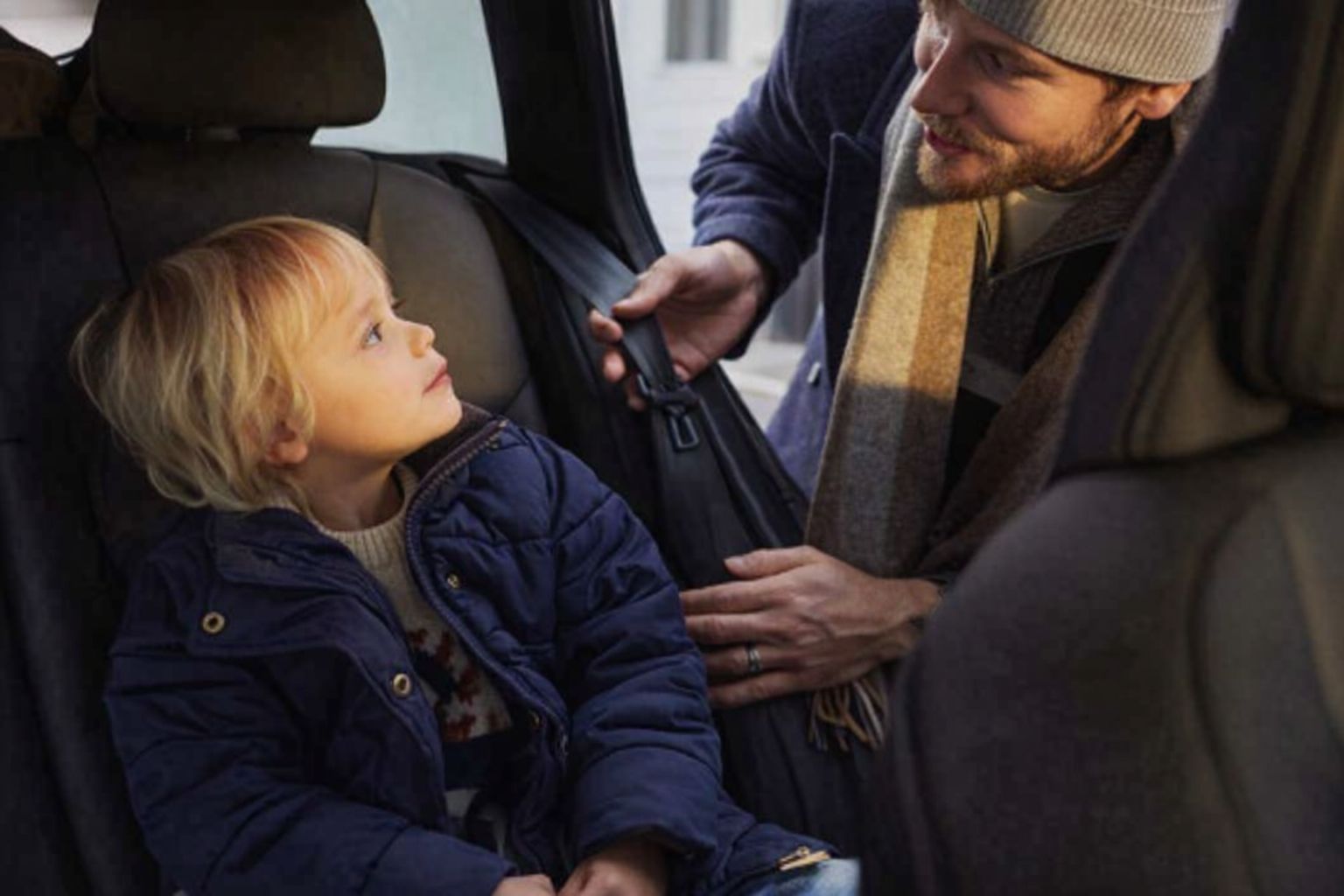 Man spänner fast barn i bilbälte på bilens baksäte, förbereder för bilresa.